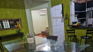A dining area with a glass table, chairs, a small potted plant, and a kitchen area with cabinets and a countertop.