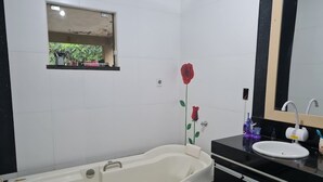 A bathroom with a bathtub, a sink, a mirror, and a small window with a view of greenery.
