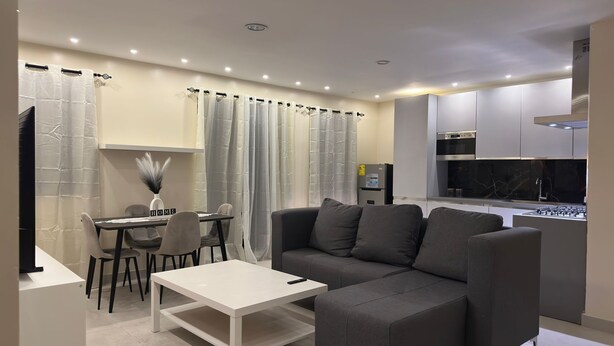 Un salon moderne avec un canapé gris, une table basse blanche et un coin repas comprenant une table et des chaises.