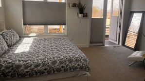 Een slaapkamer met een bed, een raam met zonwering, een deur naar een balkon en een klein plankje met decoratieve objecten.