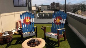 Een dakterras met twee Adirondack-stoelen, een kleine vuurkuil en een barbecue.