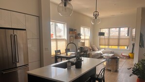 Een moderne keuken met een centraal eiland, roestvrijstalen apparatuur en een zithoek met een bank en stoelen.