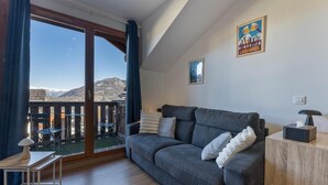 Un salón moderno con un sofá gris, una mesita de madera y vistas a las montañas a través de un ventanal.