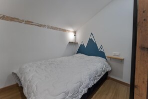 Ein Schlafzimmer mit weißer Bettdecke, einem Holzkopfende, einem Wandregal und einer Wanddekoration mit Bergspitzen.