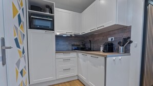 Una cocina compacta con armarios blancos, un microondas, un lavamanos y una encimera de madera.