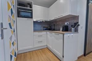 Eine kleine Küche mit weißen Schränken, einer Mikrowelle, einem Spülbecken und einer Holz Arbeitsplatte.