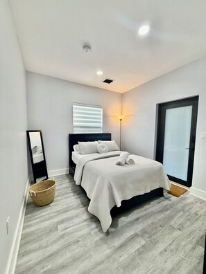 A modern bedroom with a bed, bedside lamp, and a window with blinds. - 2-bedroom townhome in fabulous Miami. (Miami)