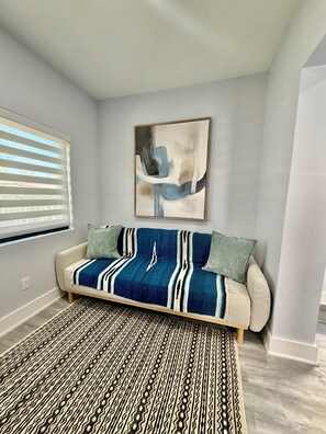 A room with a sofa, a patterned rug, a painting on the wall, and a window with blinds. - 2-bedroom townhome in fabulous Miami. (Miami)