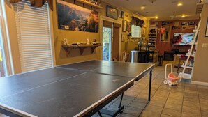 Une table de ping-pong dans une pièce dotée d’une fenêtre, d’un téléviseur et de divers éléments de décoration.