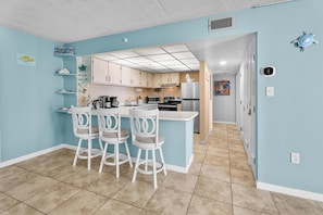 A kitchen with a central island, white bar stools, and light blue walls. - Oceanfront Condo With Pool - Steps To The Beach (Ocean City)
