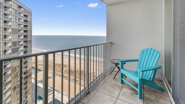 Ein Balkon mit Blick auf den Strand, ein türkisfarbener Stuhl und ein kleiner Tisch.