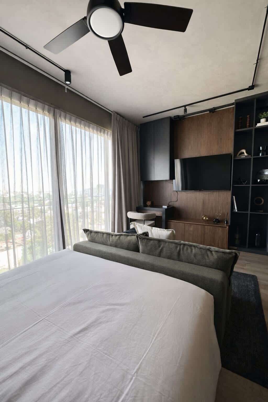 Ein modernes Hotelzimmer mit einem großen Bett, einem Deckenventilator, einem Flachbildfernseher, einem Schreibtisch und einem Kleiderschrank.