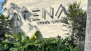 Ein Gebäudeeingang mit einem Schild, auf dem 'ATENA URBAN LIVING' steht, und einer Betonwand mit Bepflanzung.
