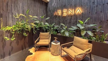 A modern lobby with a wooden wall, two leather chairs, a round side table, and a variety of plants.