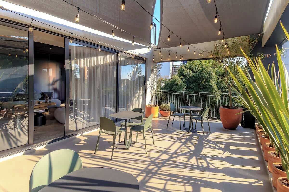 Une terrasse extérieure avec des tables et des chaises, des plantes en pot et une vue sur le paysage urbain.
