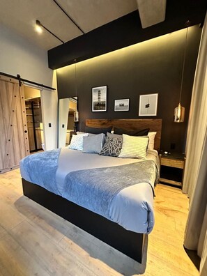 Camera moderna con un letto grande, una testiera in legno e una parete scura con quadri appesi.