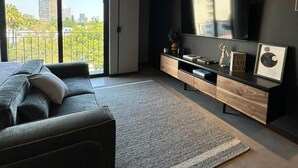Ett modernt vardagsrum med en soffa, TV och ett underhållningscenter, stora fönster och utsikt över staden.