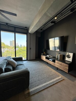A modern living room with a sofa, TV, and entertainment unit, large windows, and a city view. - Modern Apartment in Colonia Americana (Guadalajara)