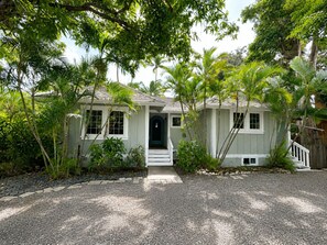 A single-story house with a front porch, surrounded by lush tropical vegetation. - Beachfront South Shore Retreat with Stunning Ocean View Deck, Surf Near Waikiki (Honolulu)