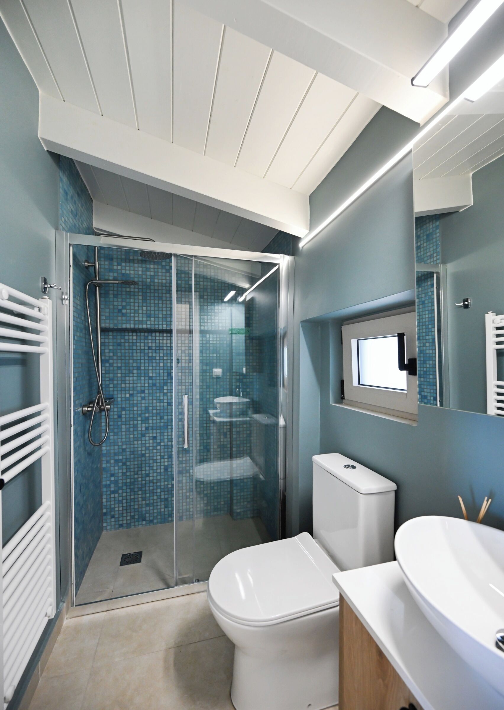 Een moderne badkamer met een douchecabine van glas, een toilet en een wastafel met spiegel erboven.