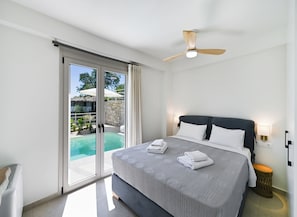A hotel room with a bed, a ceiling fan, a nightstand with a lamp, and a view of a pool through glass doors. - Maison D'Azur Lefkas Private Pool  (Lefkada)