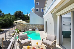 A pool area with a table and chairs, a stone wall, and a view of a building with a tiled interior. - Maison D'Azur Lefkas Private Pool  (Lefkada)