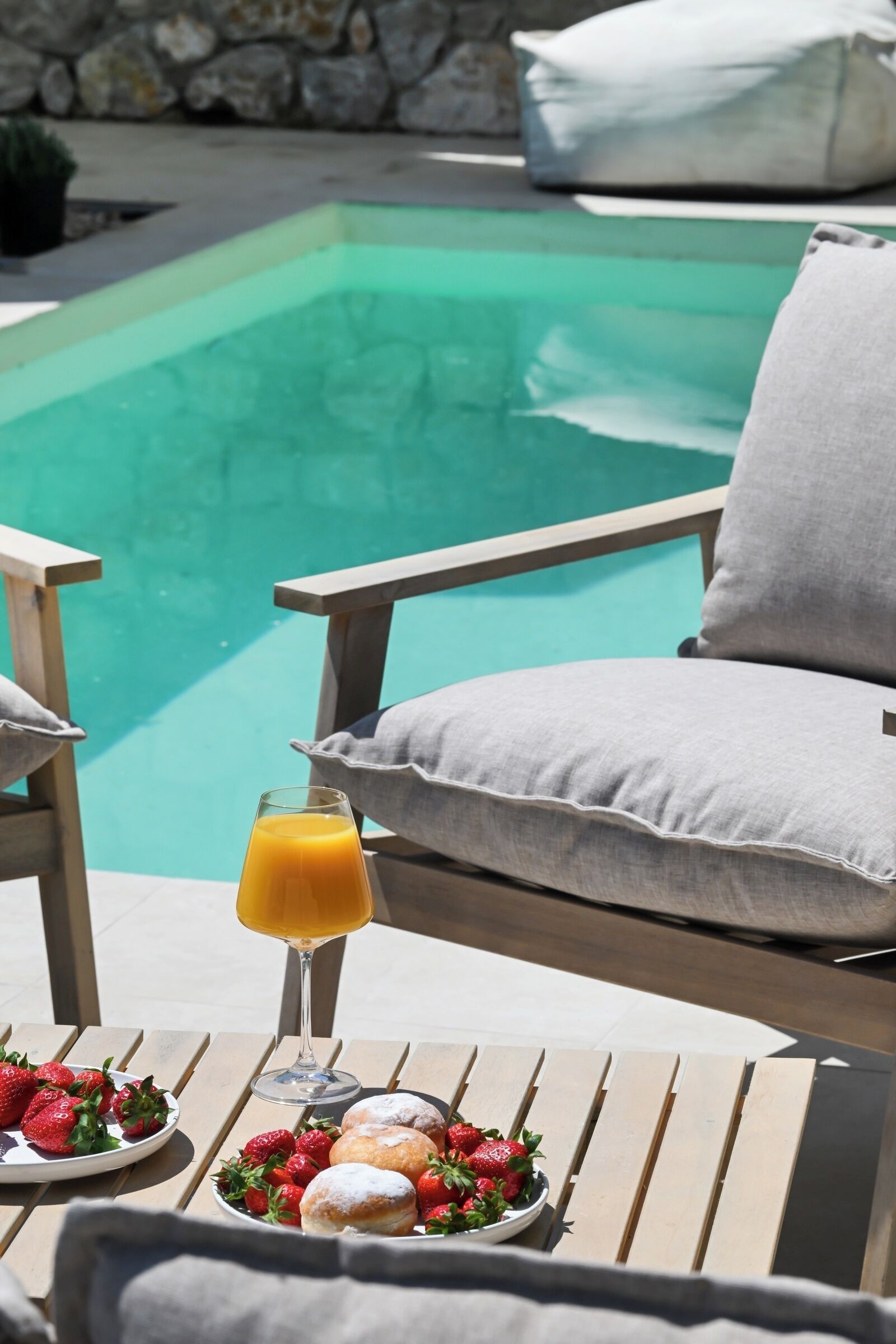 A poolside setting with a table, a glass of orange juice, and plates of strawberries and pastries.