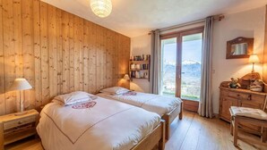 Et værelse med træpaneler, en stor seng med to puder, et sengebord med en lampe, en reol og udsigt gennem et vindue.