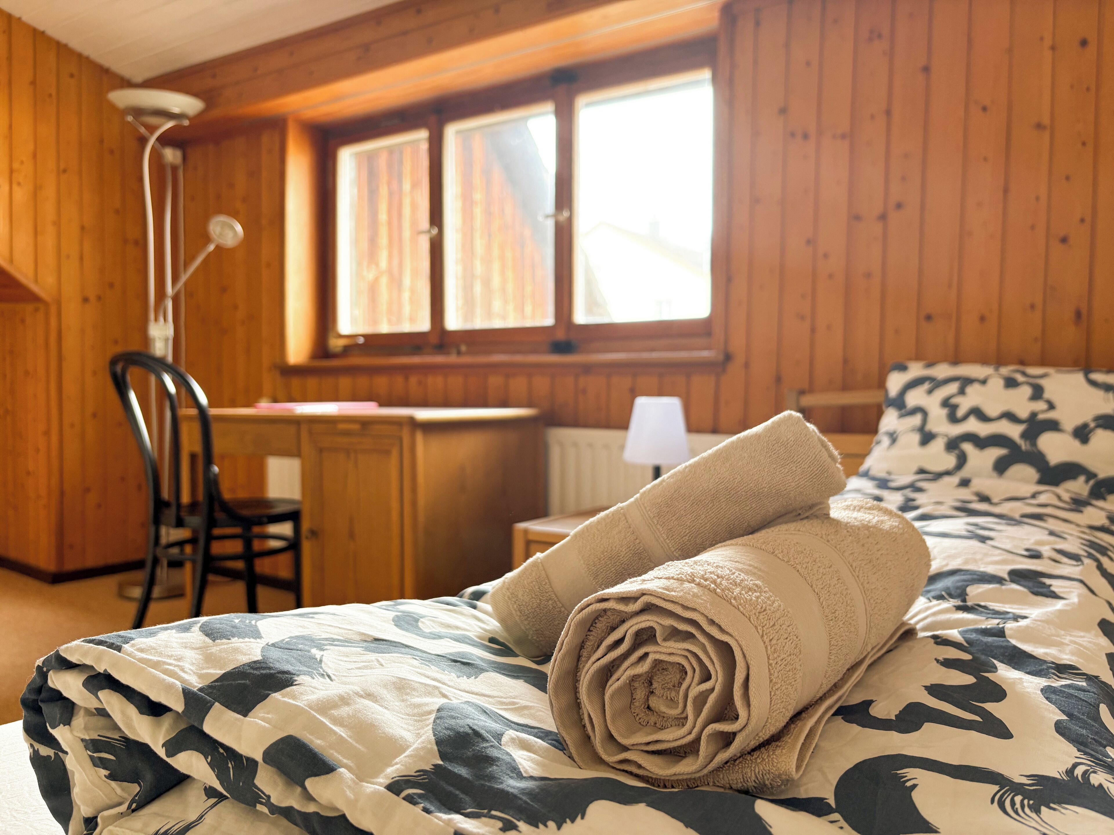 Een houten kamer met een bed, een bureau en een stoel.
