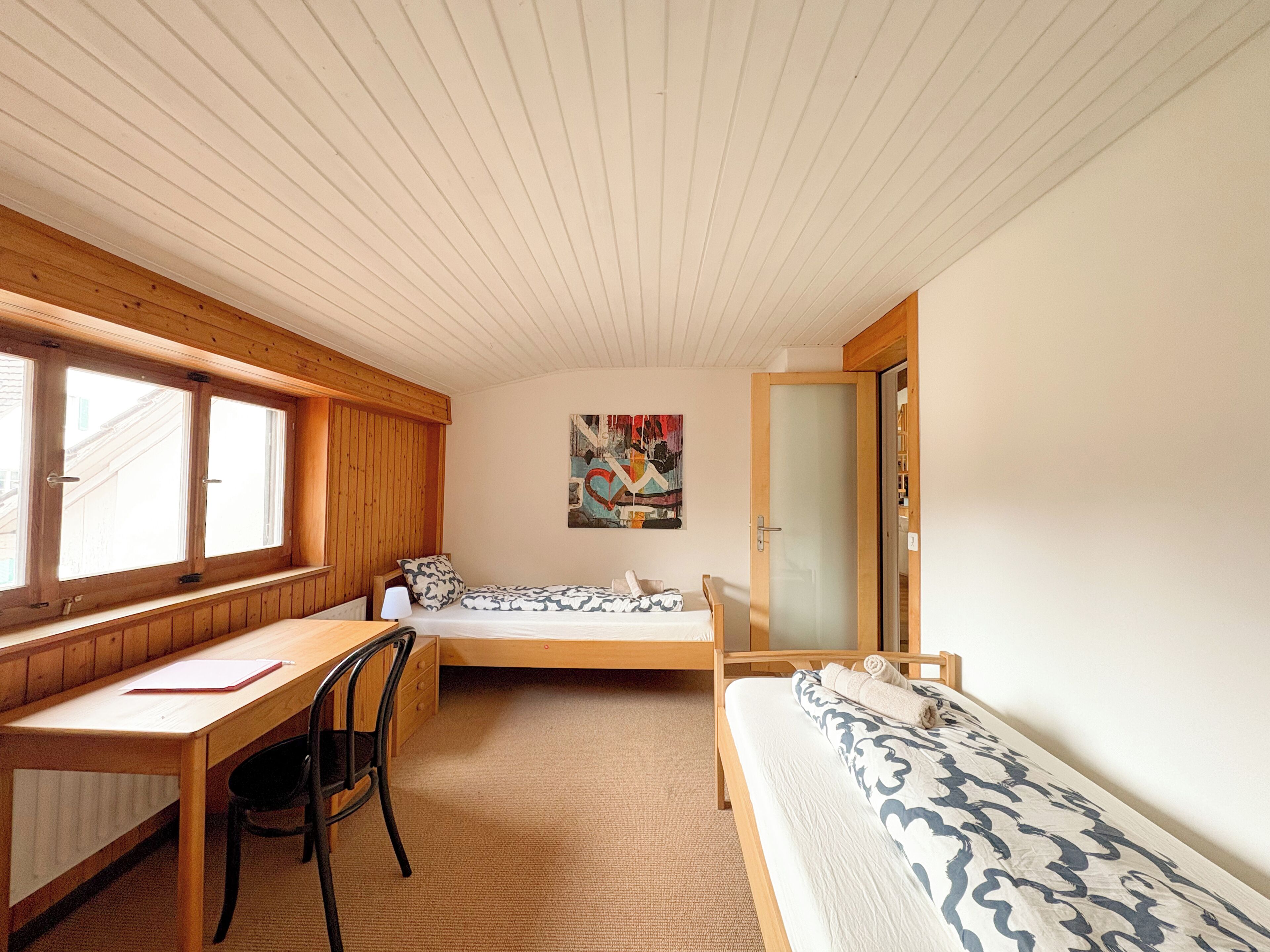 Een kamer met een bed, een bureau, een stoel en een raam.