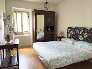 Une chambre à coucher avec un lit, une armoire, une table de chevet, une lampe et une fenêtre.