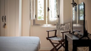 A bedroom with a bed, a chair, a desk, a mirror, and a window with curtains. - Il Casale Sotto La Torre ***(Via del Colle 21, Torano di Borgorose) (Torano)