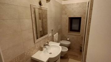 A bathroom with a sink, toilet, and bidet, tiled walls, and a small window.