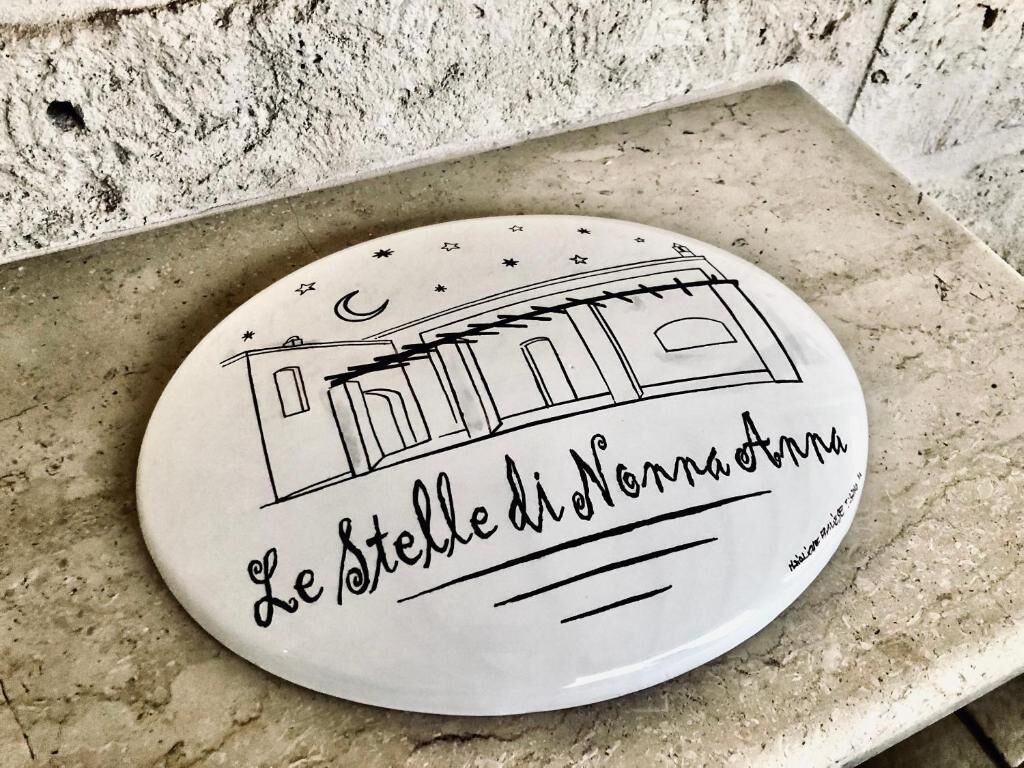 Ein weißer Teller mit einer Zeichnung eines Gebäudes und dem Text 'Le Stelle di Norma d'Anna' auf einer Steinoberfläche.