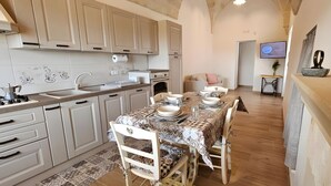 A kitchen with white cabinets, a dining table set with plates and glasses, and a TV mounted on the wall. - Le Stelle di Nonna Anna (Monopoli)