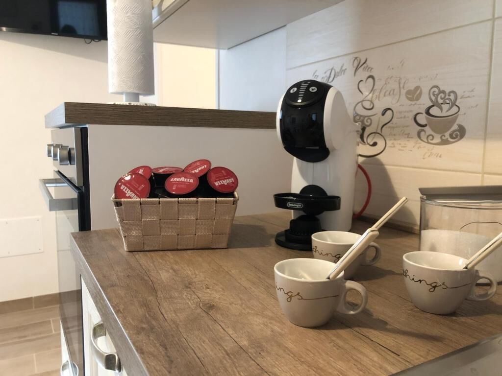 A kitchen counter with a coffee maker, a basket of red dumbbells, and several mugs with chopsticks.