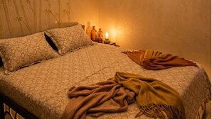 Un letto con biancheria a motivi, un comodino con delle bottiglie e una parete con carta da parati in bambù.