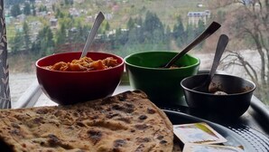 A meal with flatbread, two bowls of food, and a spoon, viewed through a window overlooking a mountainous landscape. - The himalayan Drift Cottage (Vashist)