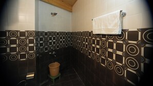 A bathroom with patterned tiles, a wooden ceiling, a towel hanging on the wall, and a trash bin. - The himalayan Drift Cottage (Vashist)