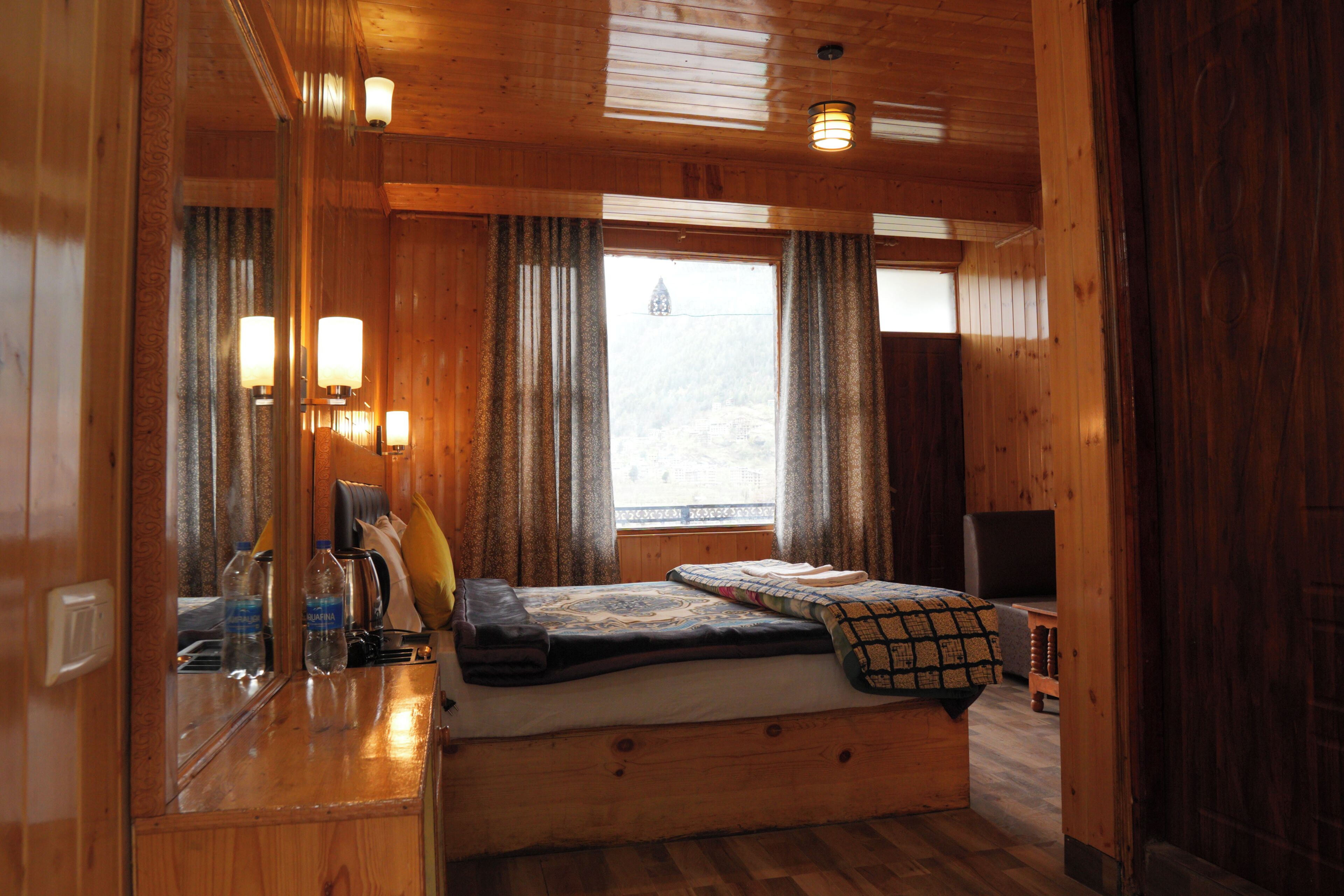 A wooden cabin interior with a bed, a small table, and a window with curtains.