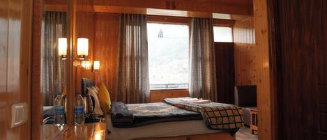 Interior de una cabaña de madera con una cama, una mesita y un ventanal con cortinas.