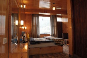 A wooden cabin interior with a bed, a small table, and a window with curtains. - The himalayan Drift Cottage (Vashist)
