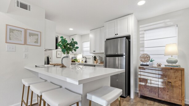 Una cocina moderna con armarios blancos, un refrigerador de acero inoxidable y una isla central con taburetes de bar.