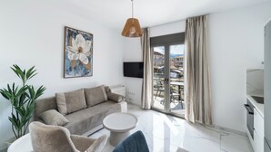 A modern living room with a sofa, a round coffee table, a potted plant, and a painting on the wall. - Urban Nest Collection Modern CityLiving  (Lefkada)