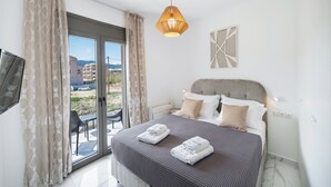 A bedroom with a bed, curtains, a hanging light fixture, a wall-mounted TV, and a view through a glass door. - Urban Nest Collection Modern CityLiving  (Lefkada)