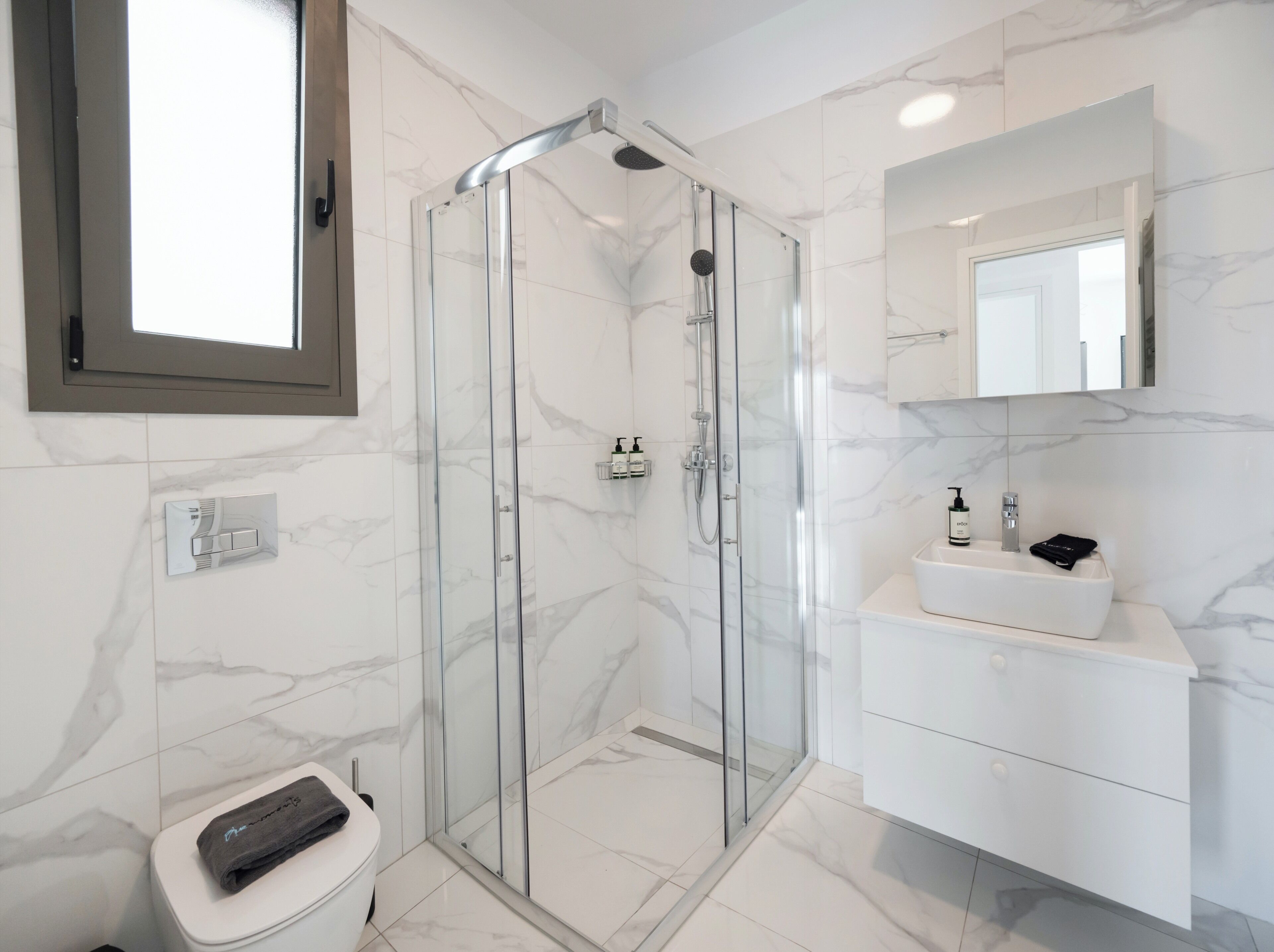 Un baño moderno con ducha envuelta en vidrio, un lavabo blanco y un espejo sobre el mueble.