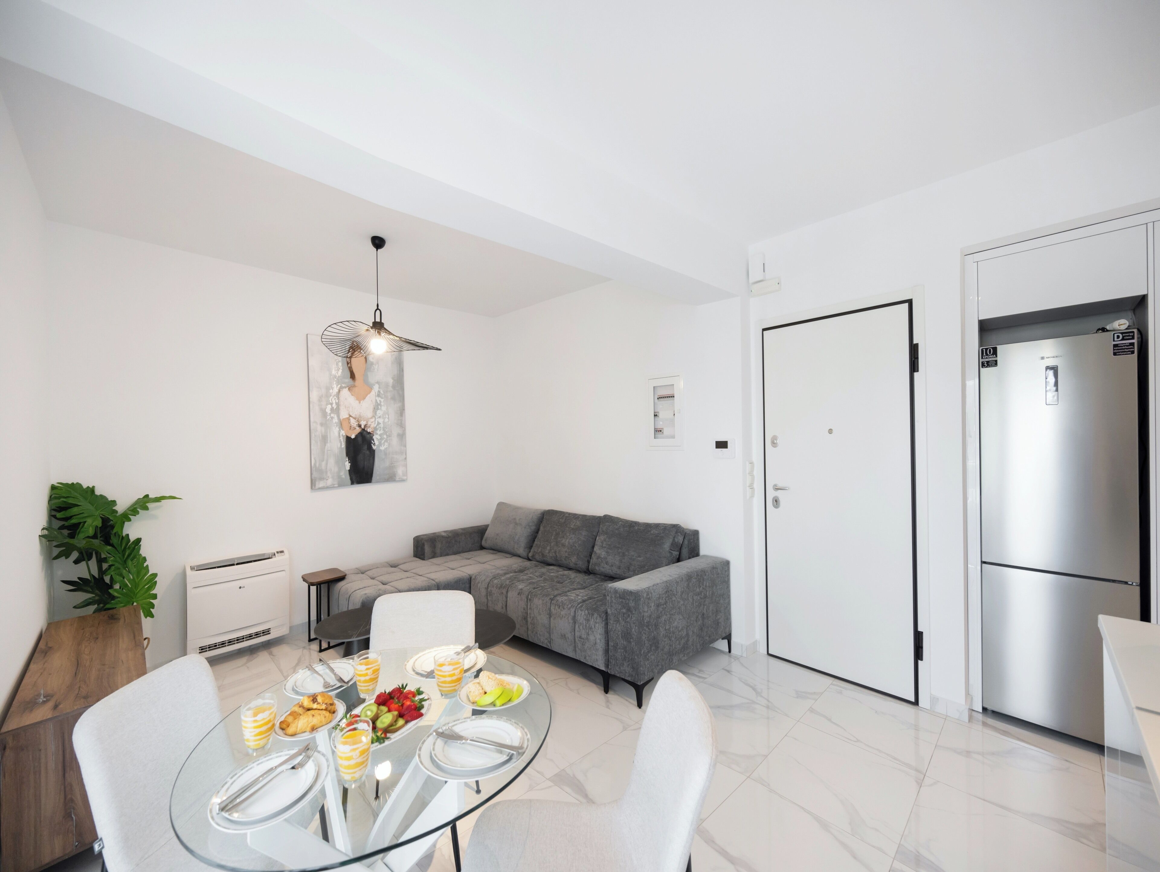 A modern living space with a glass dining table, grey sofa, and a large refrigerator.