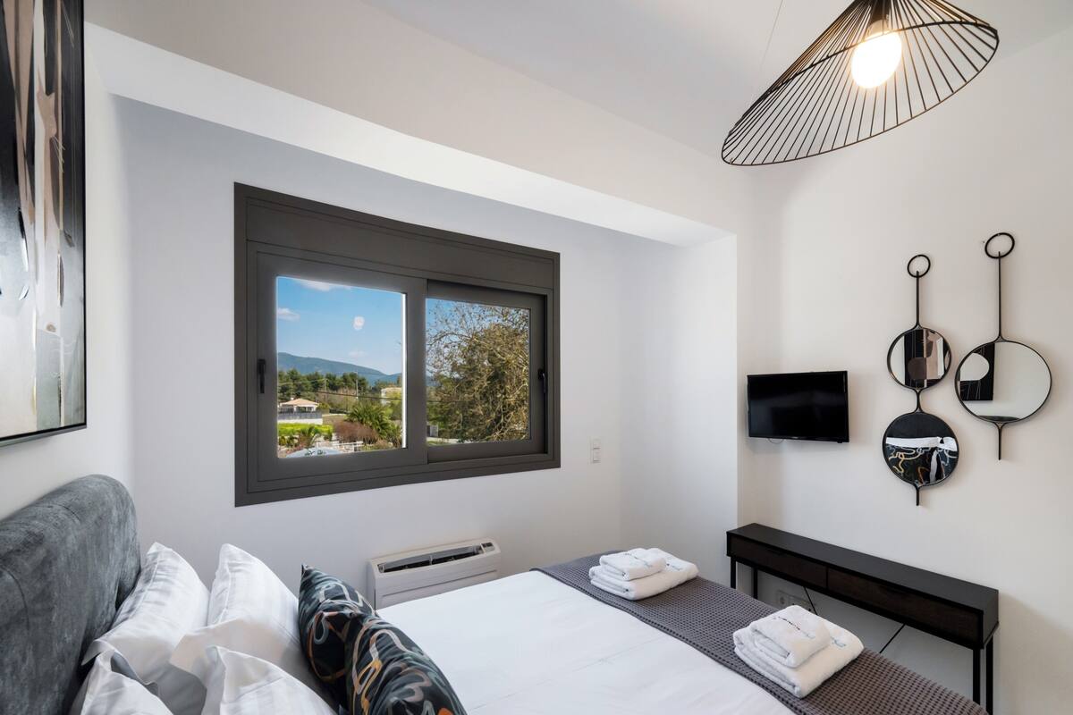 Una camera d'hotel moderna con un letto grande, una TV, una finestra con vista e un lampadario dal design originale.