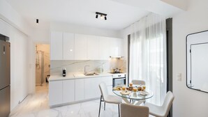 A modern kitchen with white cabinets, a glass dining table, and a breakfast setup. - Urban Nest Collection Modern CityLiving  (Lefkada)