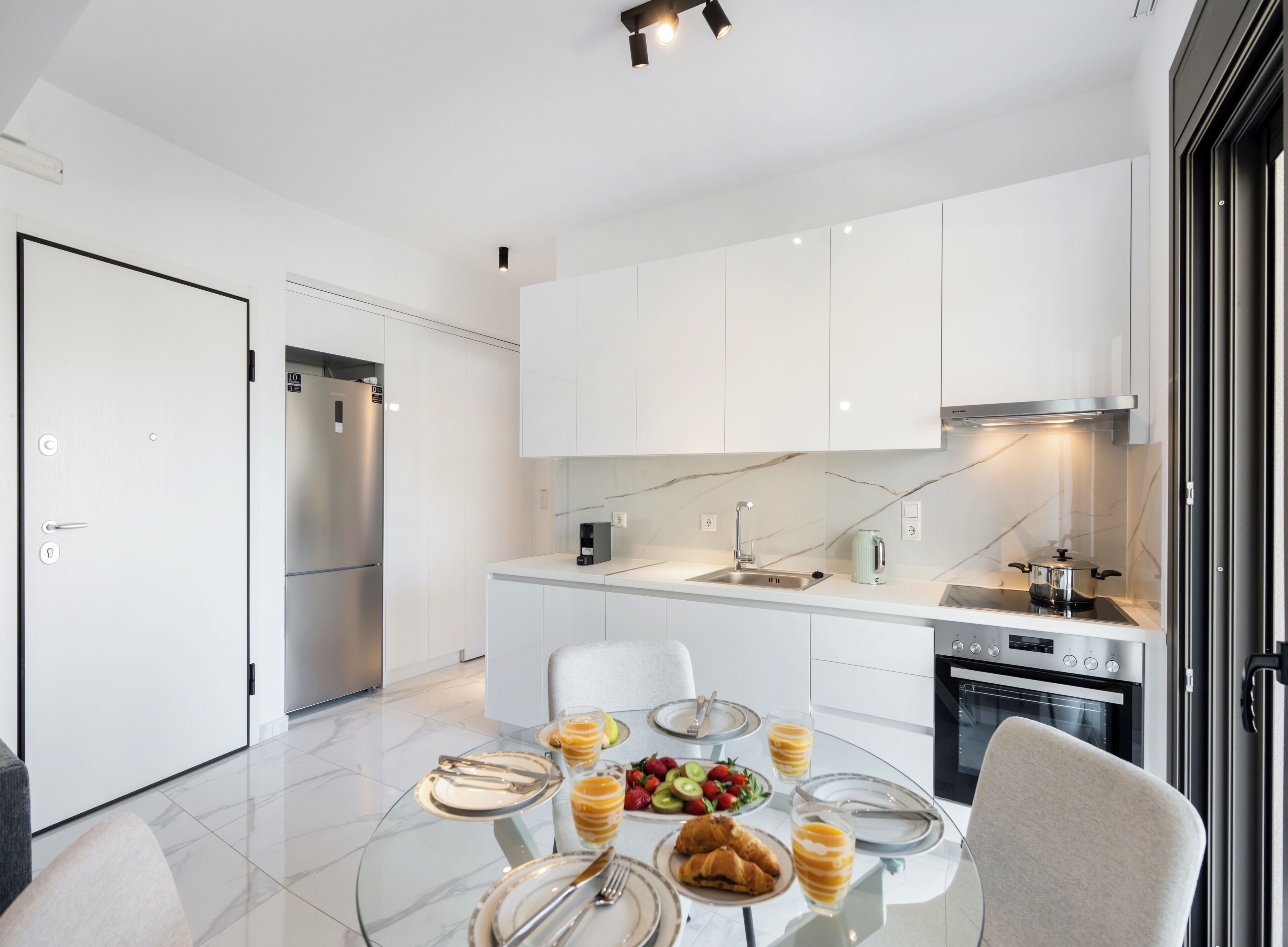 A modern kitchen with white cabinets, a built-in oven, and a dining area with a glass table set for breakfast.